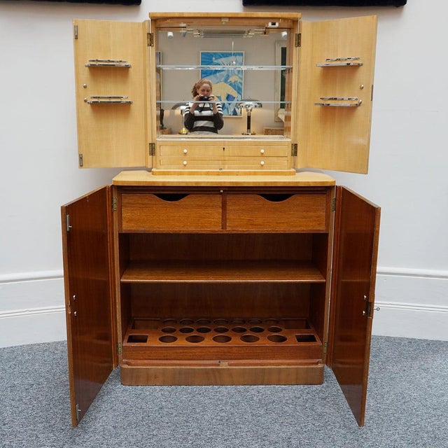 An Art Deco cocktail cabinet by Heal's of London. Two-tiered with upper mirrored interior and original handles. Heal's...