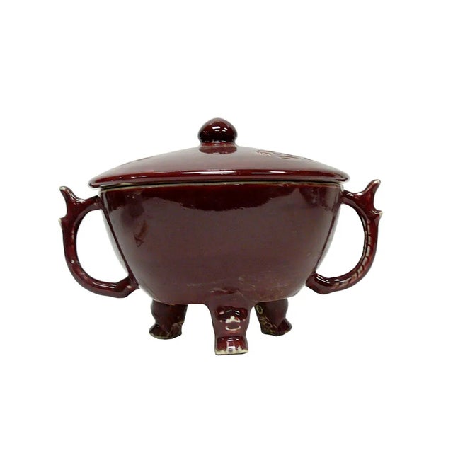 This ceramic vessel features a rich, glossy brownish-red glaze covering its exterior, complemented by two arched side...