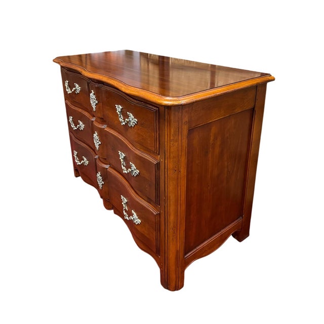 This Louis XV / French Provincial style three-drawer commode is constructed from hardwoods with a warm fruitwood and...