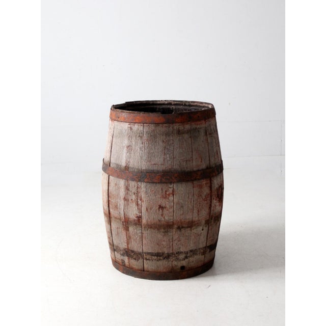 Antique wooden barrel with a tall, classic form, featuring weathered wood staves and aged iron banding. The surface...