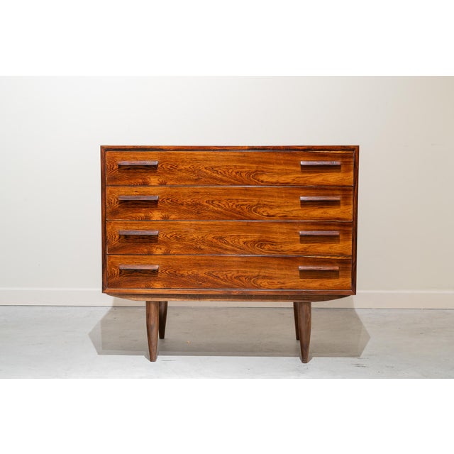 Four-drawer cabinet on a single level, supported by four legs. Each drawer has two rectangular wooden handles, and the...