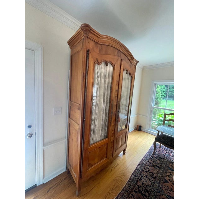 A lovely Louis XV cherry armoire with hand-hewn, glass and quarter-paneled chevron doors , an arched cornice, scalloped...