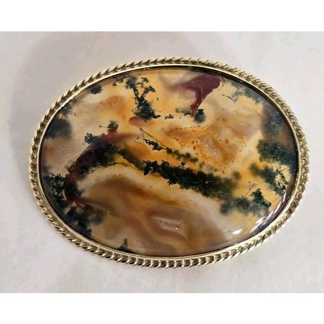 A fine vintage 9ct yellow gold brooch dating to 1989, featuring a beautifully polished oval moss agate cabochon. The...