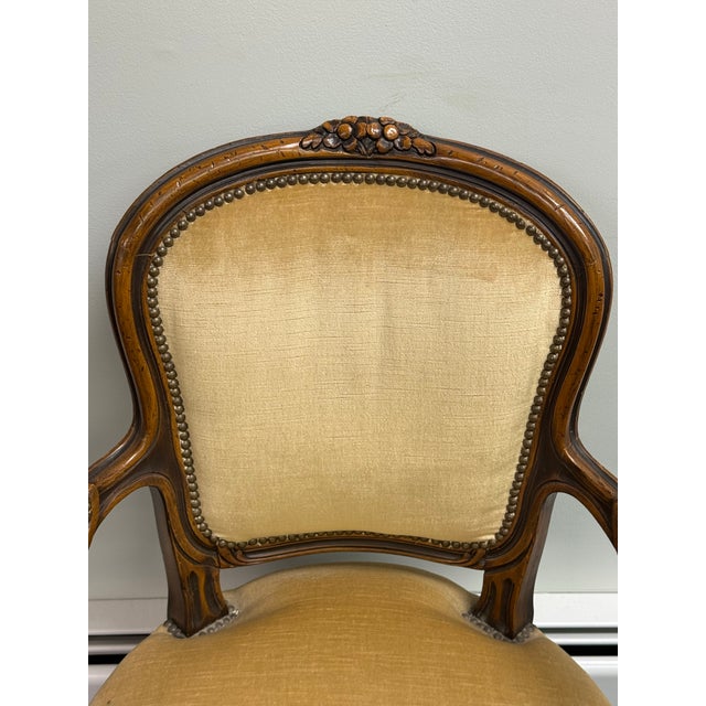 This French Louis XV-style fauteuil armchair features ornate hand-carved wood and champagne color velvet upholstery....