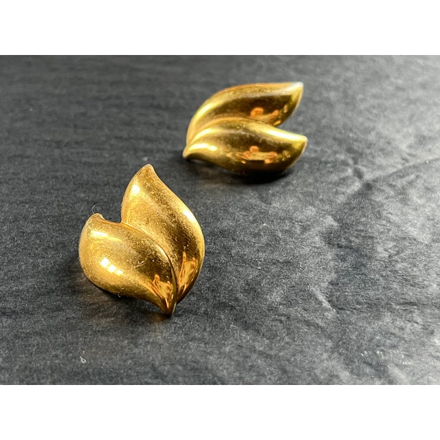 Polished gold-tone earrings designed in a fluid double-leaf motif with softly curved forms and a high-shine finish....