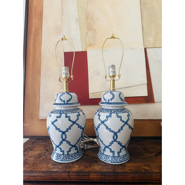 A striking pair of blue and white ginger jar lamps featuring a bold geometric lattice pattern paired with a classic Greek...