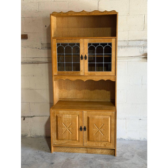 Open upper shelving sits above leaded glass doors and a lower storage cabinet with carved accents. Scalloped trim details...