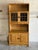 Open upper shelving sits above leaded glass doors and a lower storage cabinet with carved accents. Scalloped trim details...