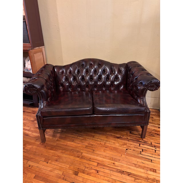 Vintage Faux Leather Settee. Tufted across the backrest and arms by detailed brass-toned nailhead trim along the front and...
