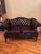 Vintage Faux Leather Settee. Tufted across the backrest and arms by detailed brass-toned nailhead trim along the front and...