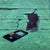 This acrylic painting presents a detailed portrayal of a mouse poised near a classic wooden trap, set against a textured...
