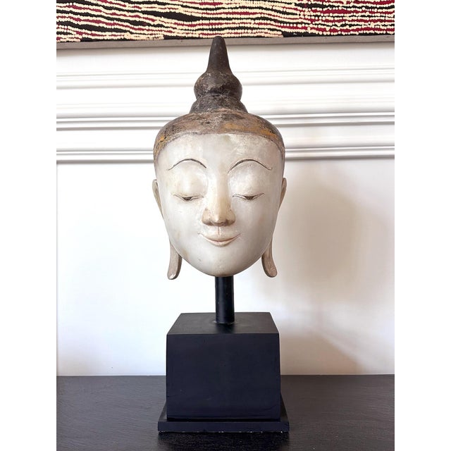 A large life-size statue of Buddha head carved from a single block of white alabaster marble and painted with gold and...