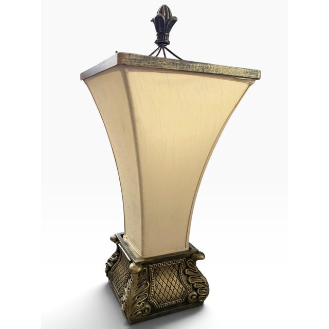 A striking vintage table lamp with an ornate neoclassical-inspired design and warm antique gold-tone finish. The...