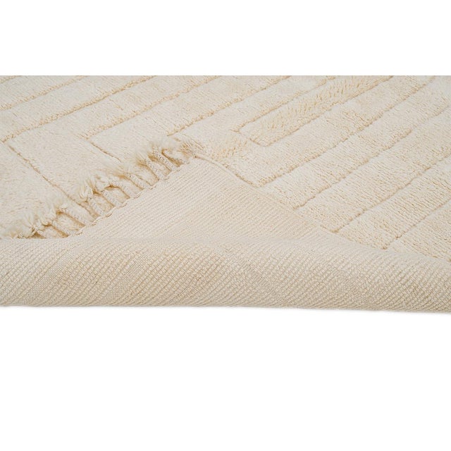 Textured hand-knotted wool rug showcases a concentric rectangular pattern in soft Ivory tones. Its minimalist design and...