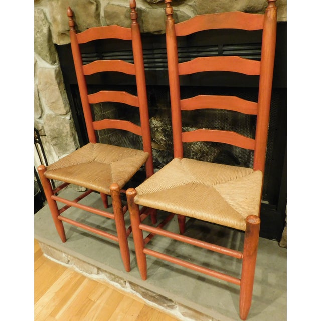 A handsome pair of traditional ladderback chairs featuring a deep red wood finish that enhances the natural grain and...