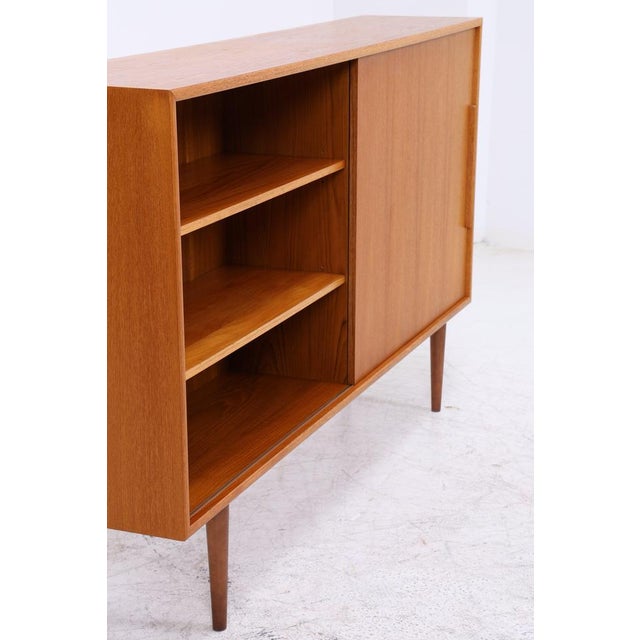 Vintage highboard from WK Möbel with clean lines and warm teak grain. The large sliding door can be moved from either...