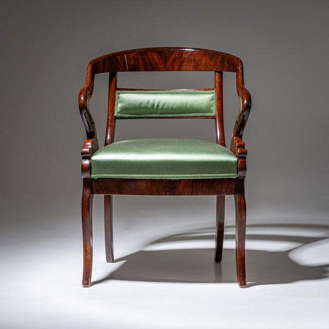 Mahogany armchair with a rounded backrest and S-shaped armrests terminating in stylized dolphin heads. The seat and...