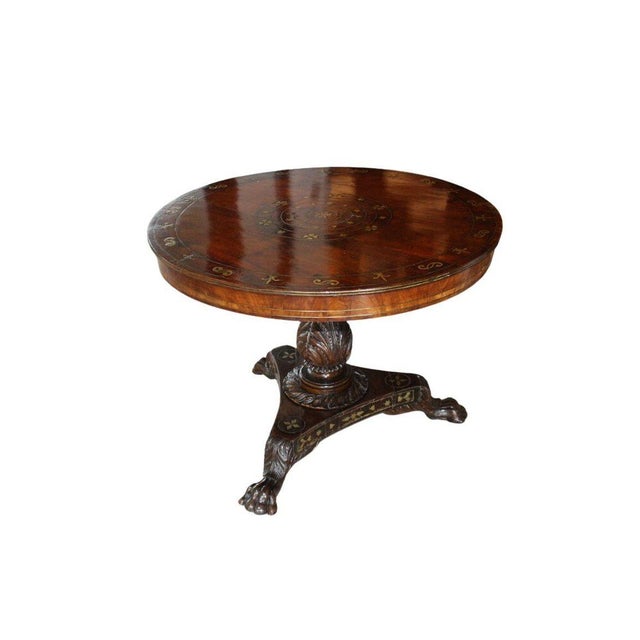 A striking antique pedestal center table dating to the early 19th century, featuring richly toned wood, decorative brass...
