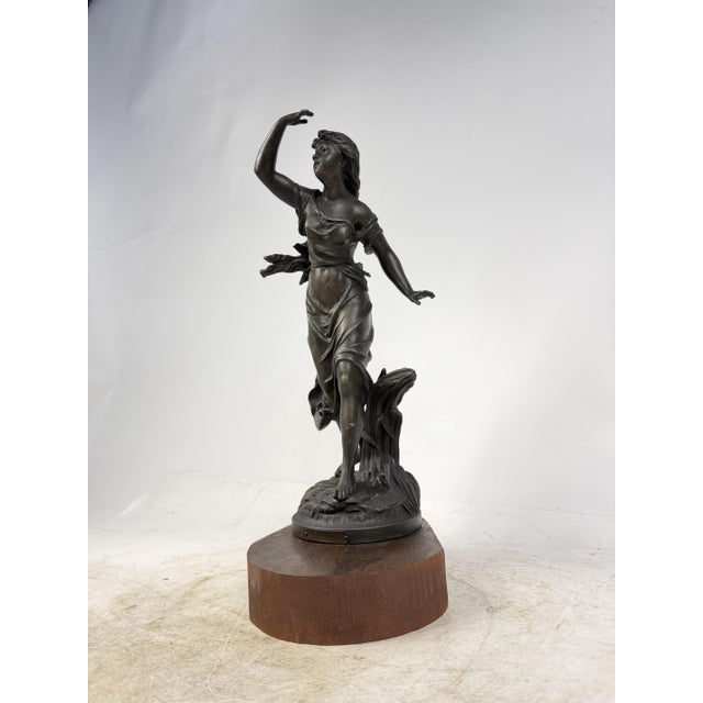 A refined patinated bronze sculpture depicting a young girl, resting on a wooden base. The work stands out for its elegant...