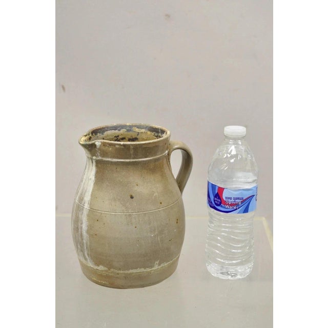 Antique Primitive Stoneware Salt Glazed 8" Bulbous Water Pitcher with Handle. Circa Late 19th Century. Measurements: 8" H...