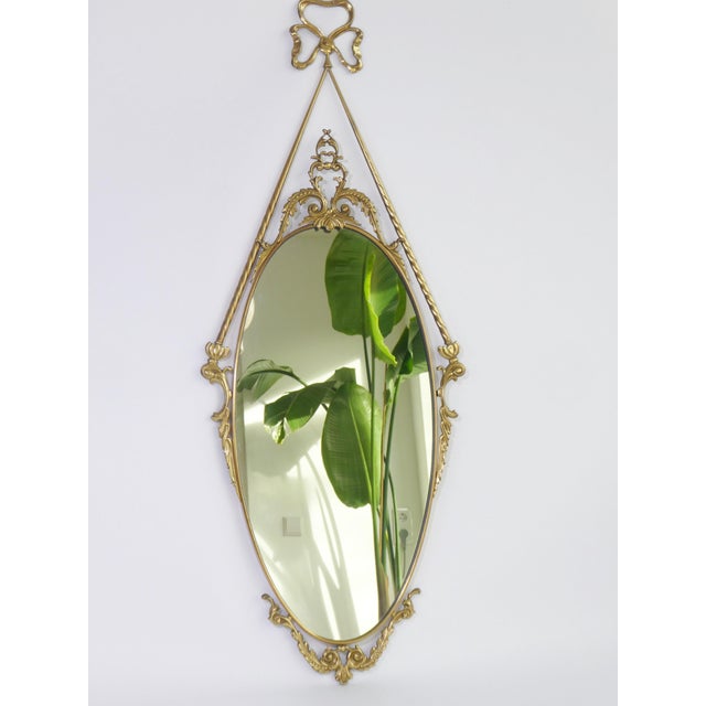 A vintage oval wall mirror with an ornate brass frame made in Italy. The mirror has stunning decoration around the frame...