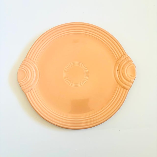 A large vintage Fiestaware cake serving plate in an apricot glaze. Features a lovely circular embossed pattern and handles...