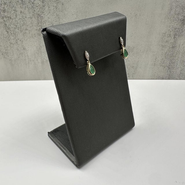 These elegant emerald and diamond dangle earrings in 10kt yellow gold feature approximately 6x4mm pear cut green emeralds...