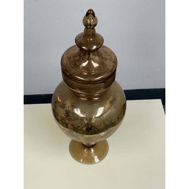 Design Plus Gallery presents an Antiqued Mercury Glass Footed Lidded Jar. The rounded glass vessel rests upon a circular...
