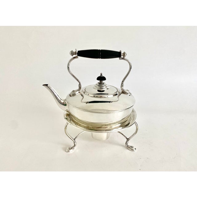 This English silverplate kettle with ebonised finial and handle sitting on a stand with four cabriolet legs and burner was...
