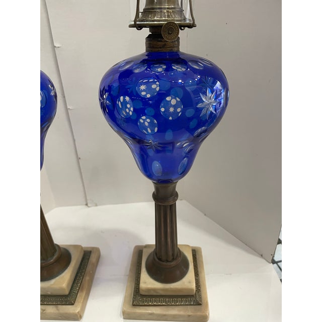 The product is a pair of antique Victorian-style oil lamps made of cut-to-clear cobalt blue glass, brass, and marble....