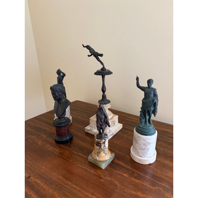 A refined collection of Grand Tour–style brass figures mounted on richly varied marble bases, each piece evoking the...