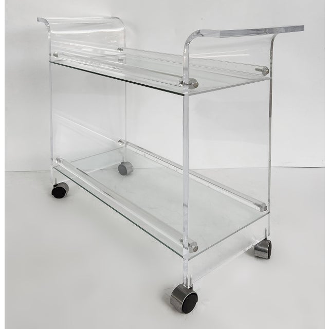 Mid-century Modern Lucite 2-tiered Rolling Bar/Serving Cart on Casters Offered for sale is a striking Lucite and acrylic...