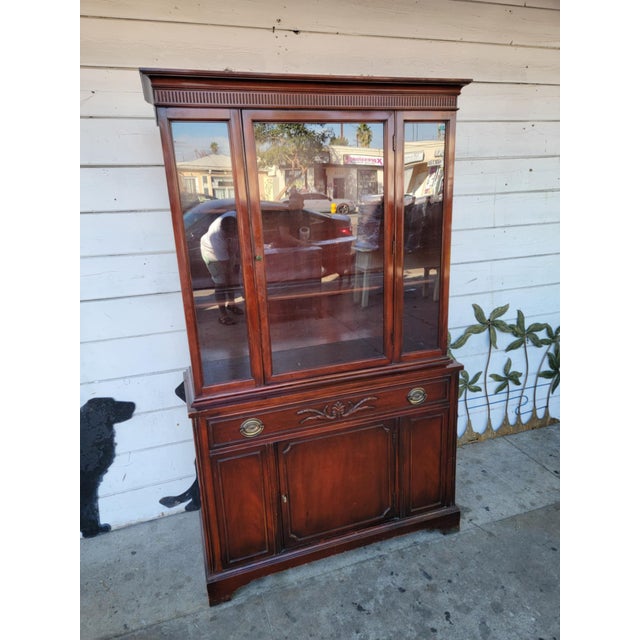 1980's vintage traditional mahogany wood China cabinet. Bottom has a cabinet, single door and a drawer. upper has a glass...