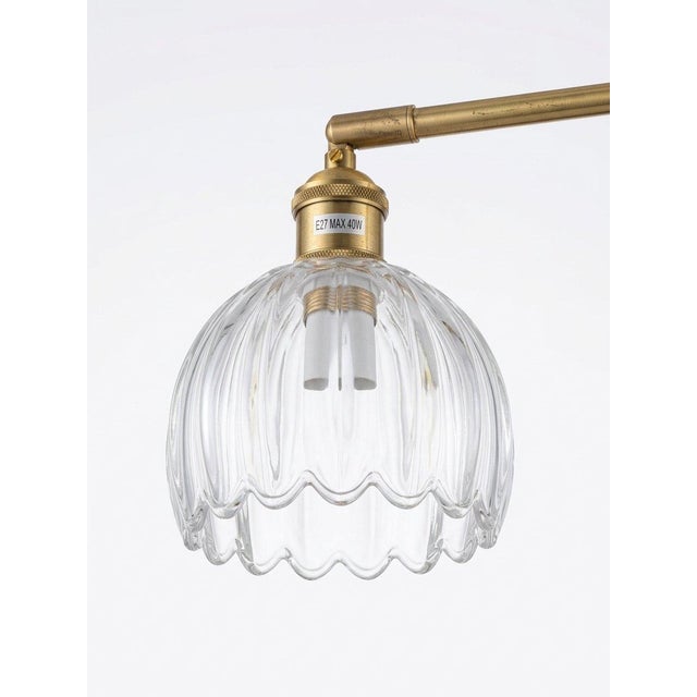 An elegant wall light featuring a warm antique brass finish paired with a beautifully shaped clear ribbed glass shade. The...