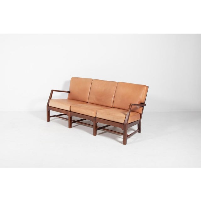 This elegant Danish Modern sofa has an architectural slat back stained wood frame fitted with loose cognac leather...