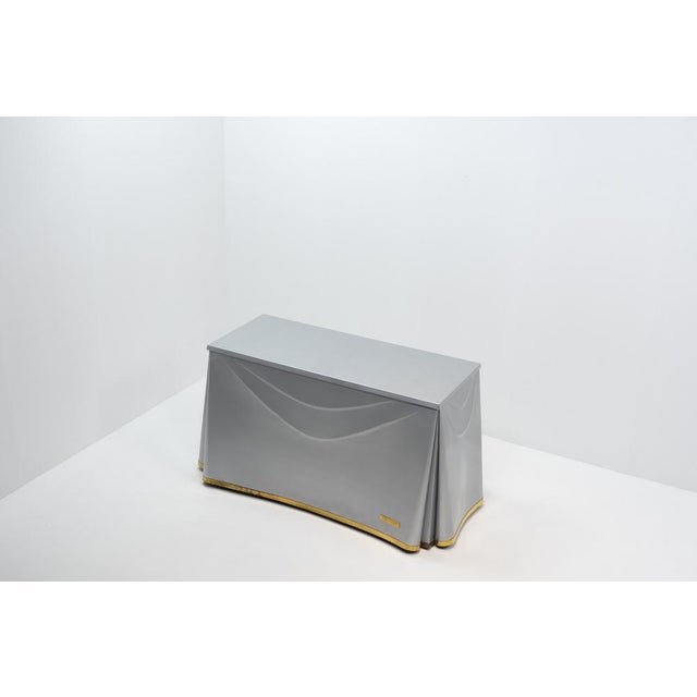 This sculptural table by John Dickinson is crafted from galvanized steel, meticulously formed to resemble flowing draped...