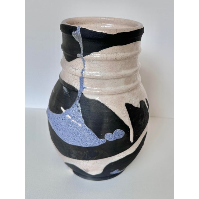 This striking handmade pottery vase features a dynamic interplay of black and white glazes with a distinctive blue accent....