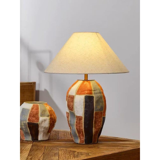The lamp base is made of ceramic, featuring color-block texture with orange, brown and gray tones, paired with a beige...
