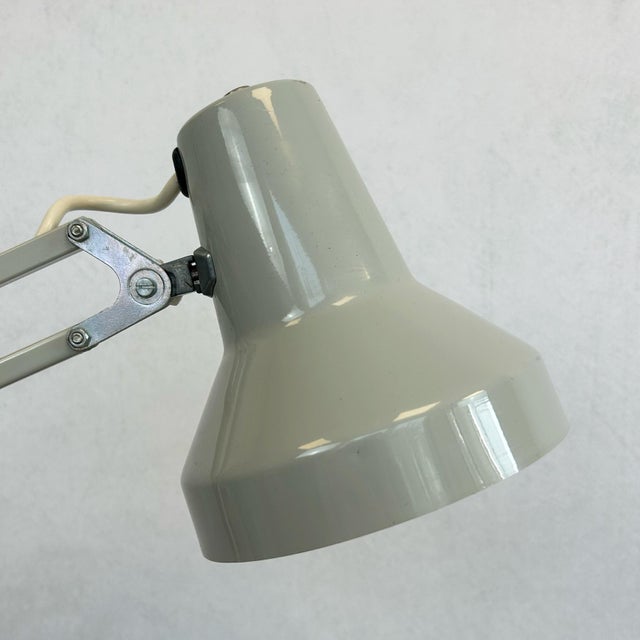 Grey architect's desk lamp with tapered shade, articulated double arm, and clamp-on base. Features geometric triangular...