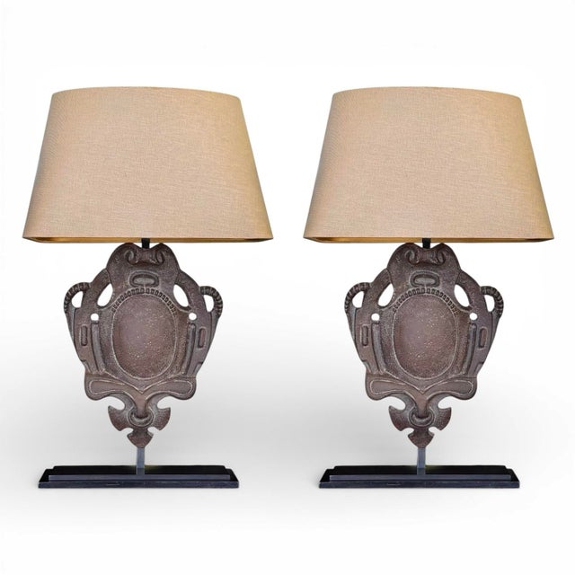 A substantial pair of iron table lamps; each featuring a large textural cast iron shield in an antique finish mounted to...