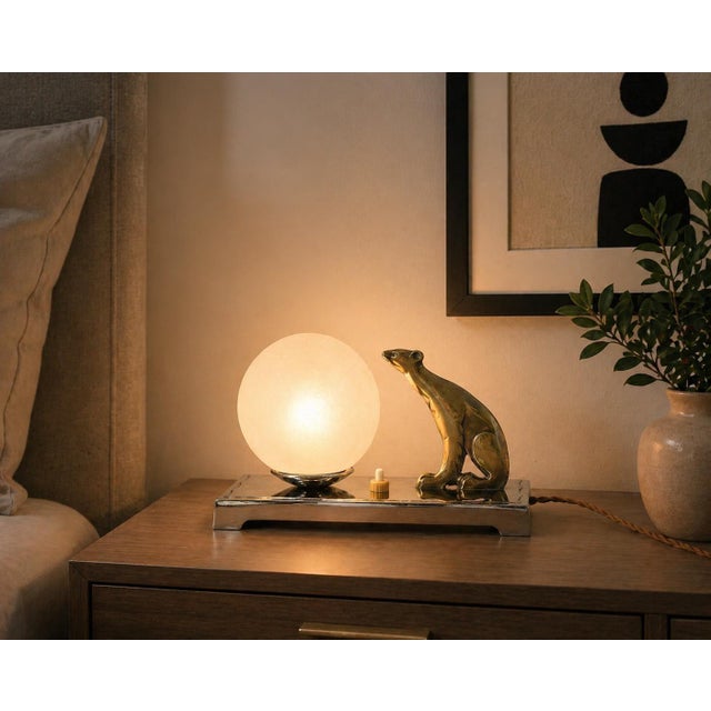 Compact Art Deco table lamp dating to the 1940s. A stylised animal figure in a brass-toned finish sits upright beside a...