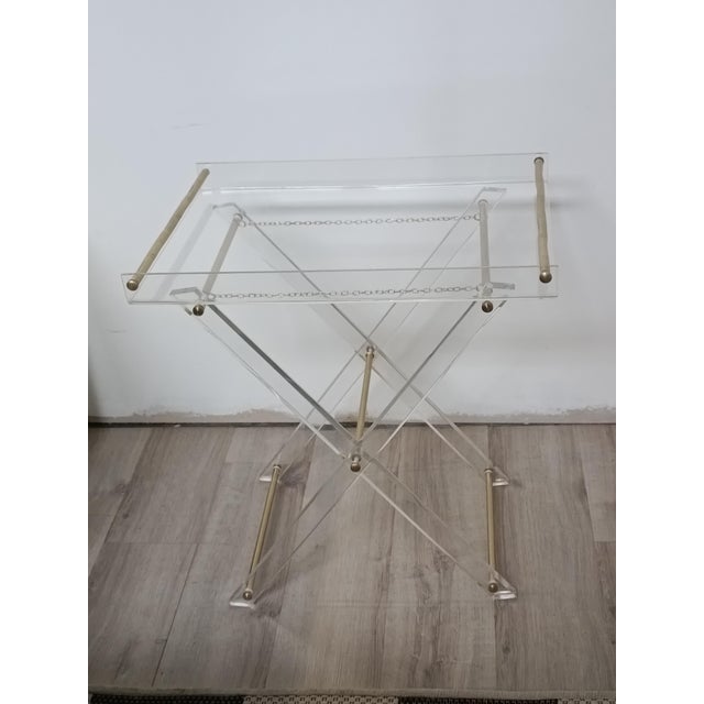 Beautiful folding side table. Italy, 1970s. Acrylic glass frame. Brass details, tubes, and chains. The X-shaped base...