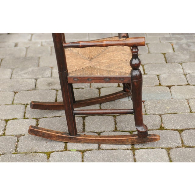An English Georgian period plum wood child's rocking chair from the early 19th century, with rush seat, ladder back and...