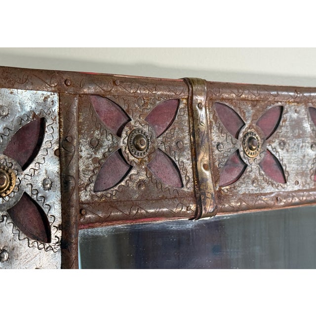 This wall mirror features a rectangular glass mirror set within a patchwork cut metal frame with raised Moorish style red...