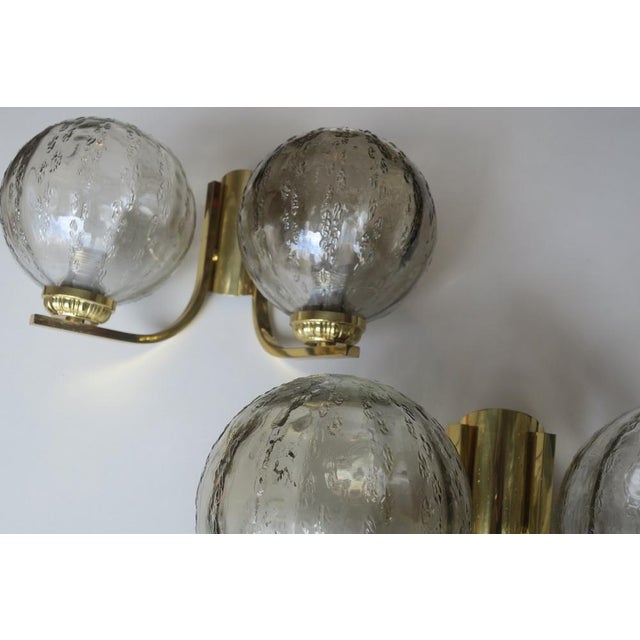 A pair of double wall lights from the 1970s, each with two globes in structured glass on a brass frame. Up to 250V...
