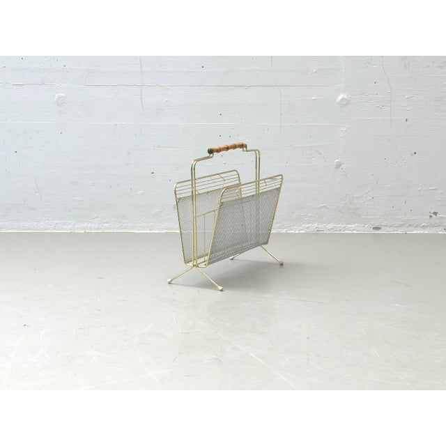 Elegant vintage magazine rack made of lacquered metal with a finely crafted wire mesh and a decorative wooden handle. The...