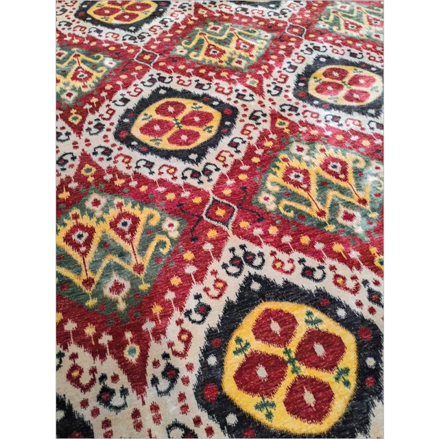 Hand-knotted rug with vibrant red and black, featuring a traditional geometric Ikat pattern with diamond and circular...