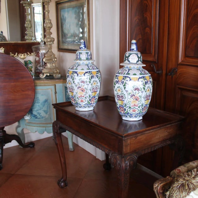 A colorful pair of large octagonal faceted tin glazed Delftware jars with flared and domed lids surmounted by lion...