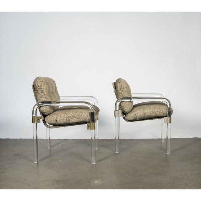Late modern lounge chairs combining clear lucite arms and legs with polished metal framing and graphic woodgrain-patterned...