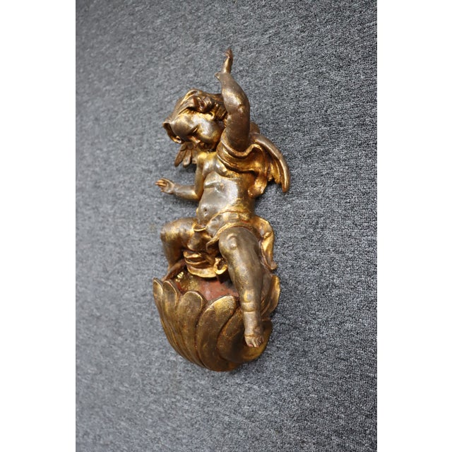 Carved giltwood wall bracket featuring a winged cherub seated atop a fluted pedestal. Richly detailed with a distressed...